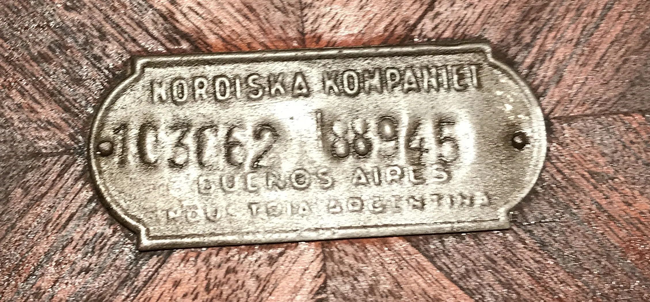 प्लेट प्राचीनता के साथ सीरियल नंबर 10306288945, पृष्ठभूमि लकड़ी की है।