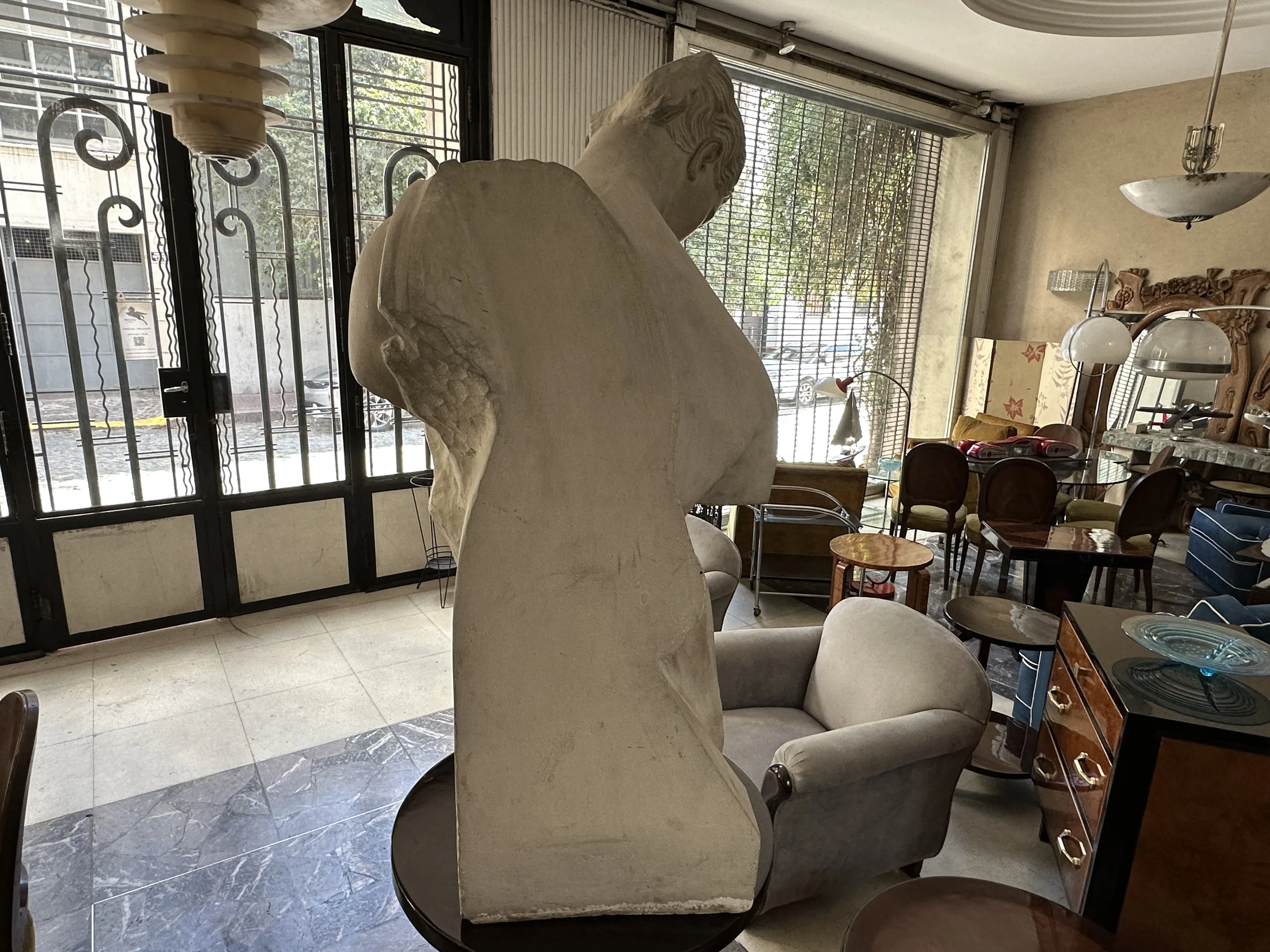 Vista lateral de una escultura antigua de Pietro Barzanti en un entorno decorativo con muebles variados y luz natural.