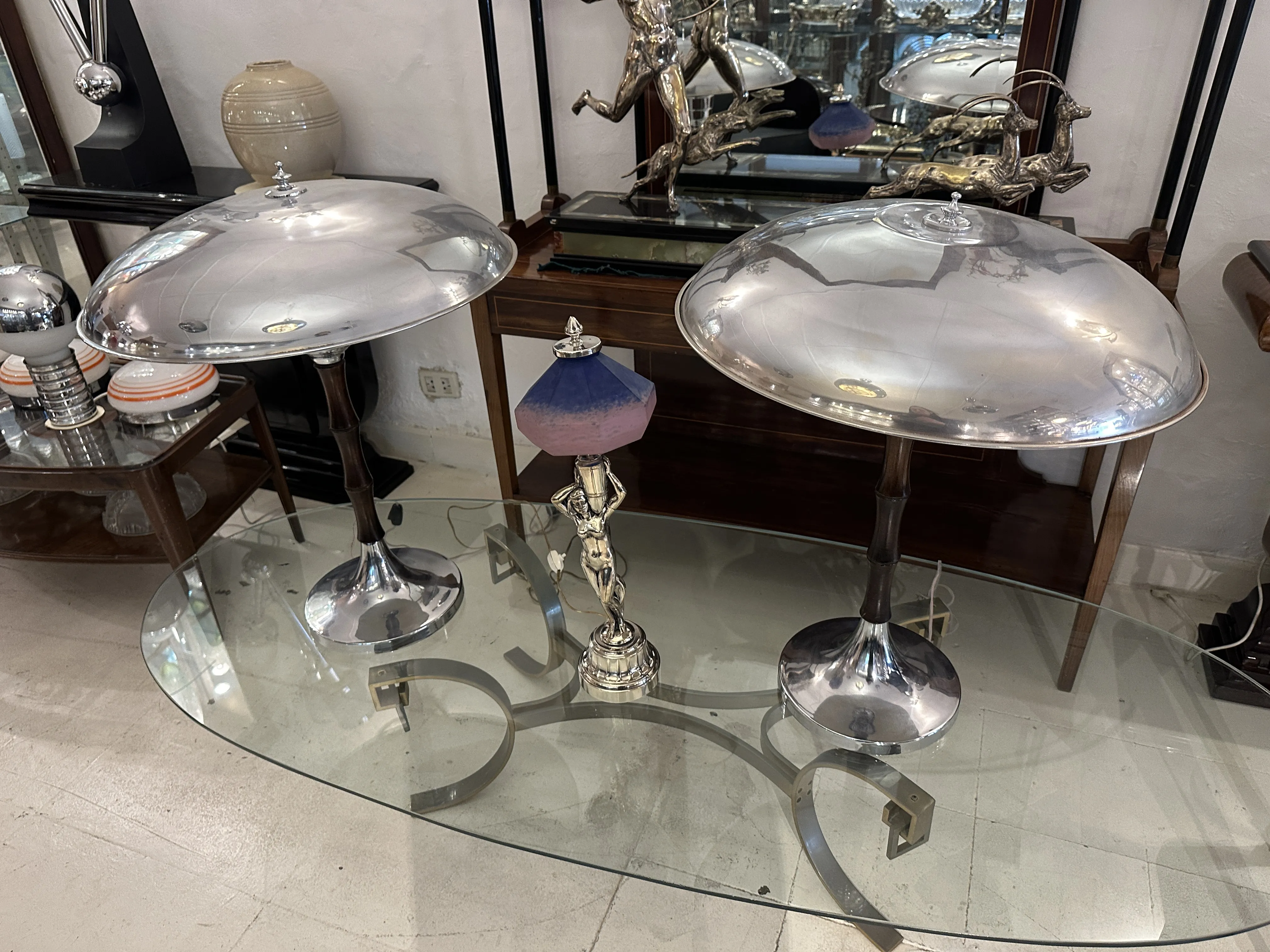 ガラスのテーブルの上に置かれた2つの光沢のあるアンティークテーブルランプ、他の装飾品に囲まれています。