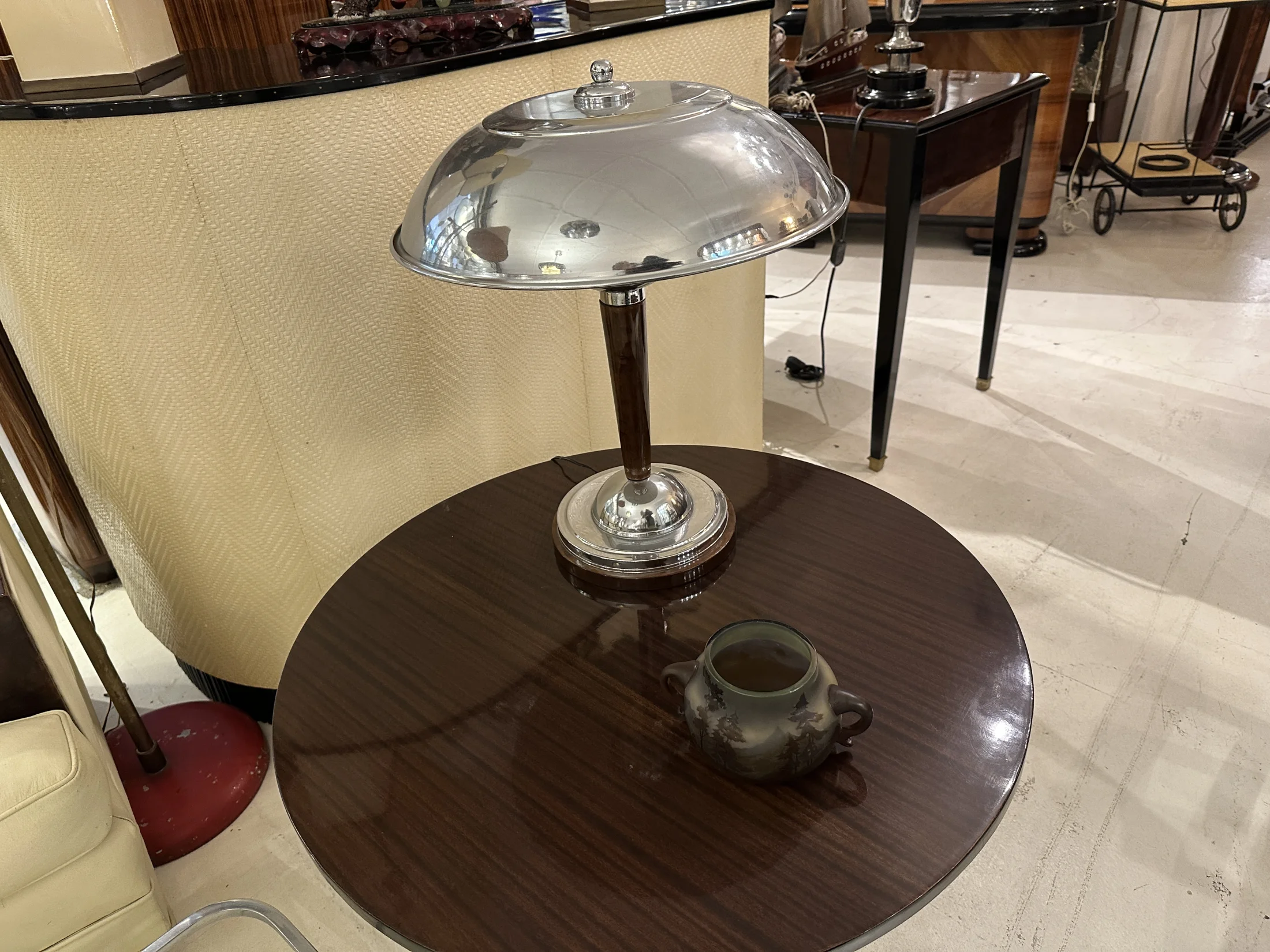 An antique desk lamp on a round wooden table with a decorative vase in a cozy setting.