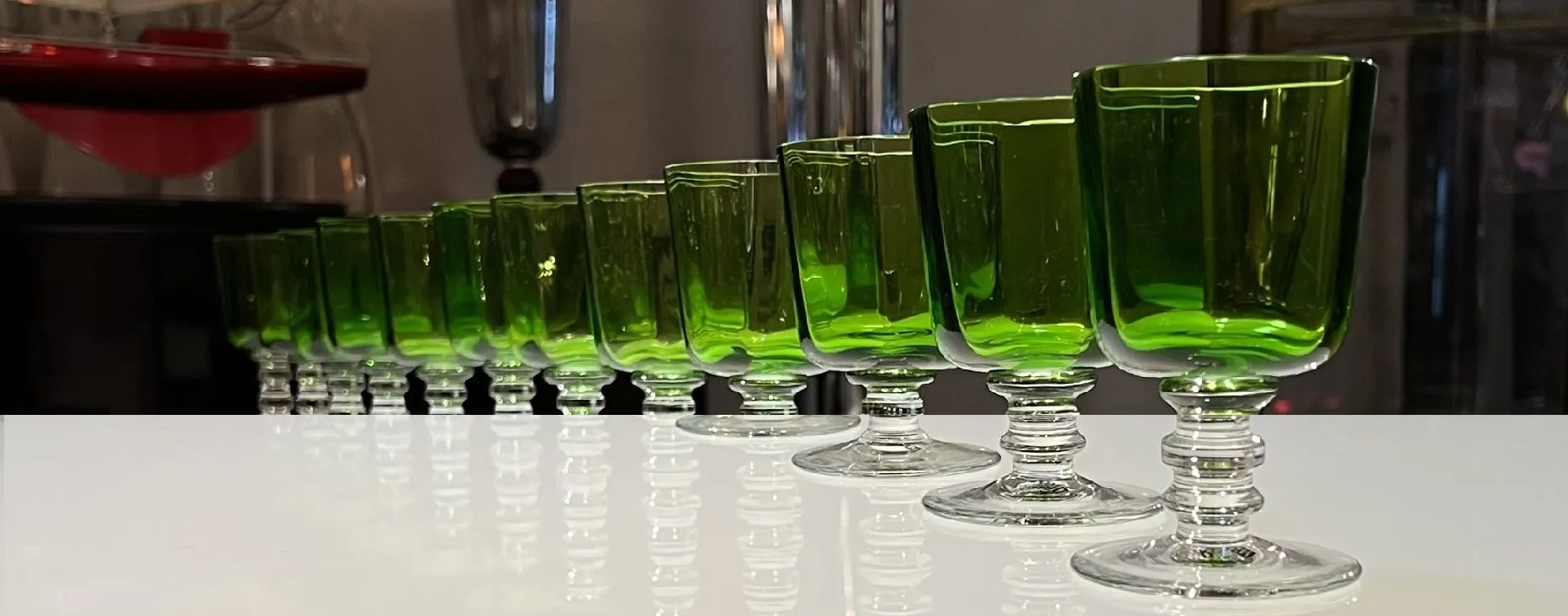 古董绿色酒杯在白色桌面上排成一行，投射出微妙的阴影。