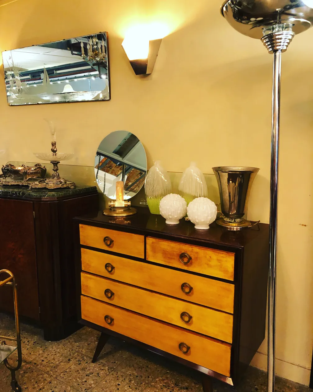 Gaveteira antiga com acabamentos em madeira em tons amarelos, decorada com objetos de vidro e metal.