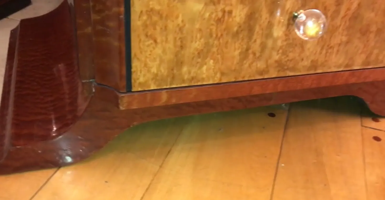 detail of an antique cabinet with an elegant design and crystal handle, on wooden flooring.