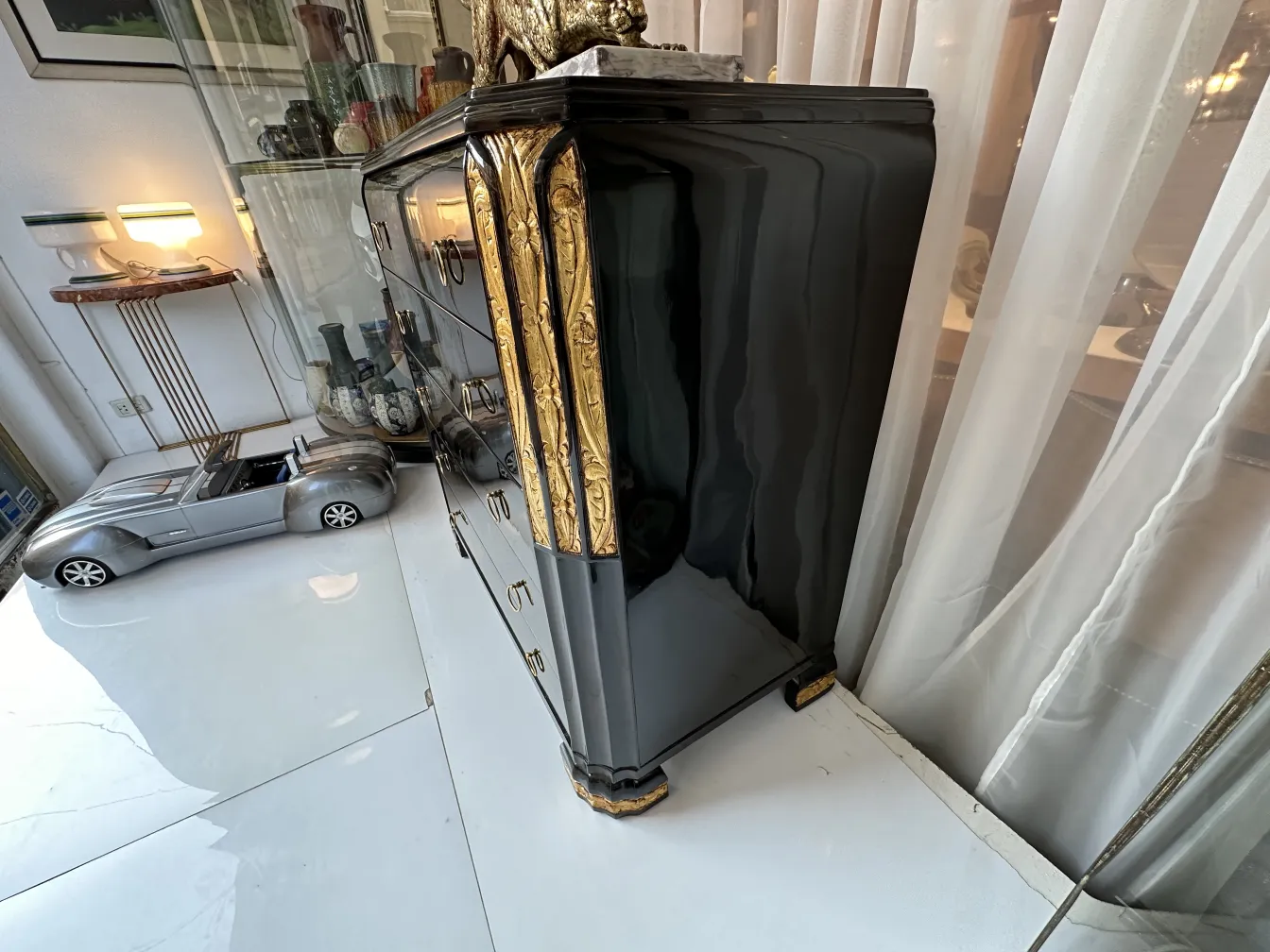 Gaveteira antiga com design elegante e detalhes dourados, acompanhada de um carro de brinquedo e objetos decorativos.