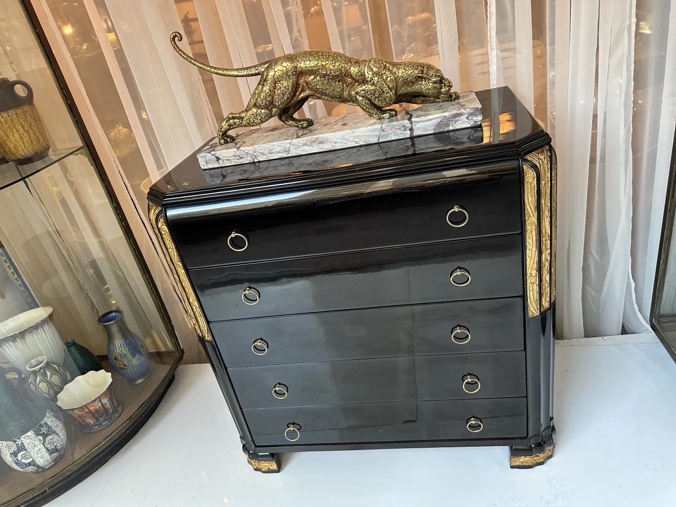 Gaveteira antiga com acabamento preto e detalhes dourados, decorada com escultura de felino.