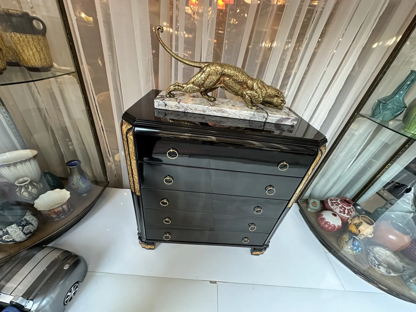 Cassettiera antica nera con decorazione in bronzo, circondata da collezioni decorative.