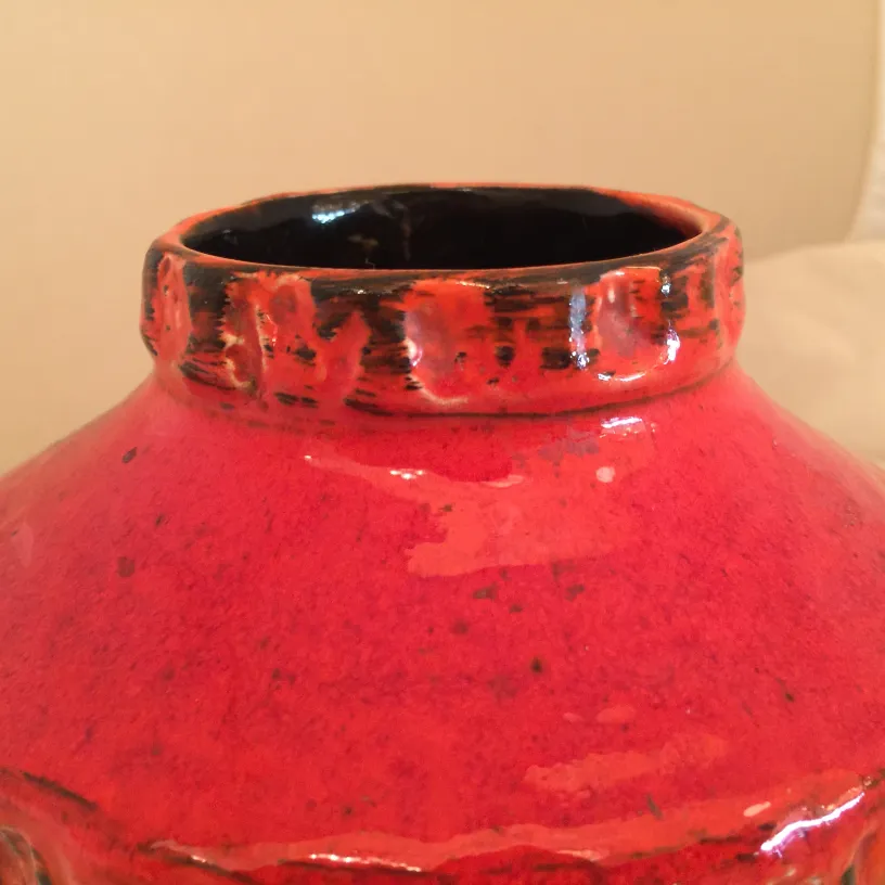 Ancienne céramique rouge brillante avec des détails noirs et des décorations subtiles en haut.