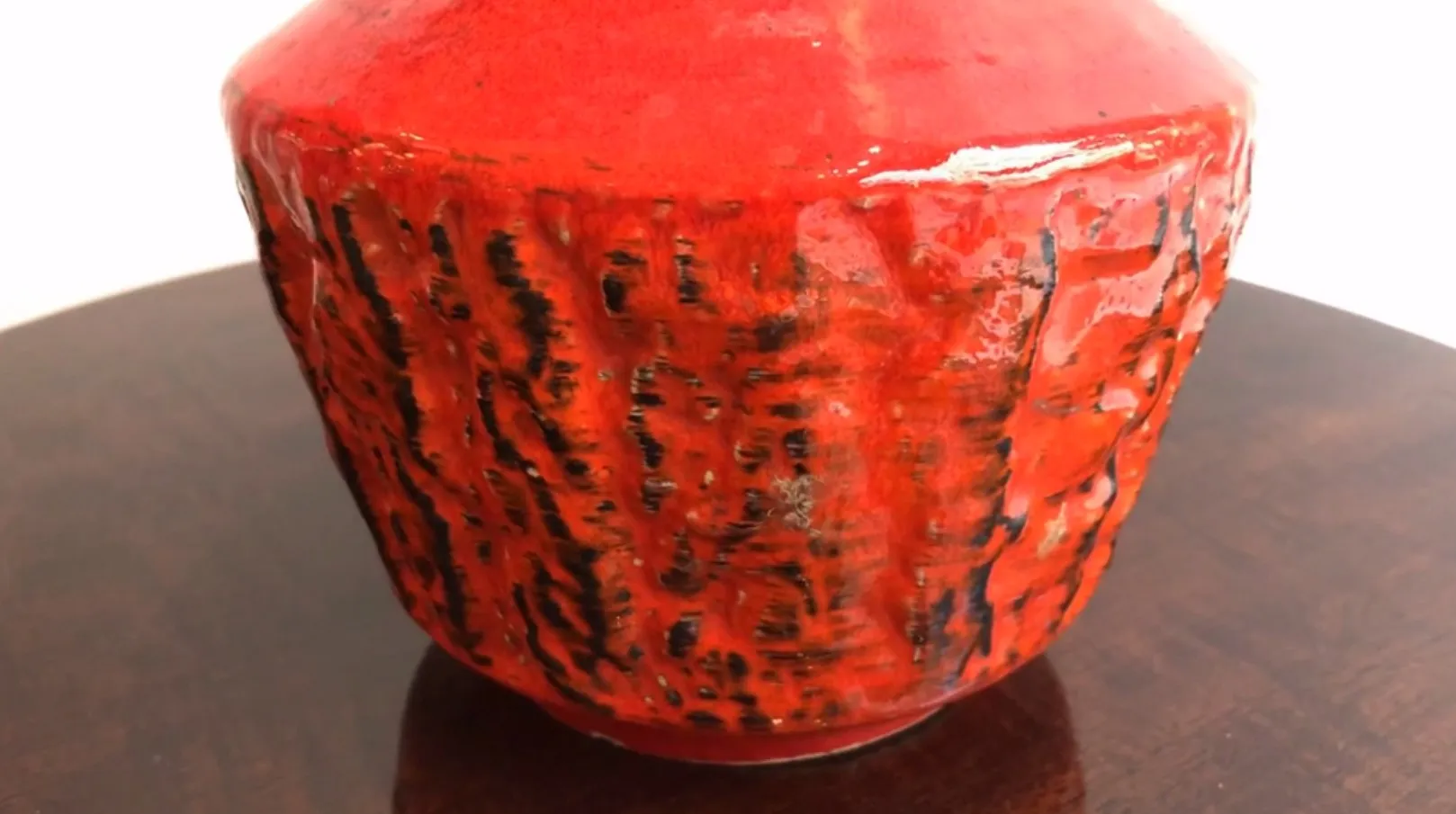 Vaso di ceramica rossa antica con texture unica su sfondo scuro.