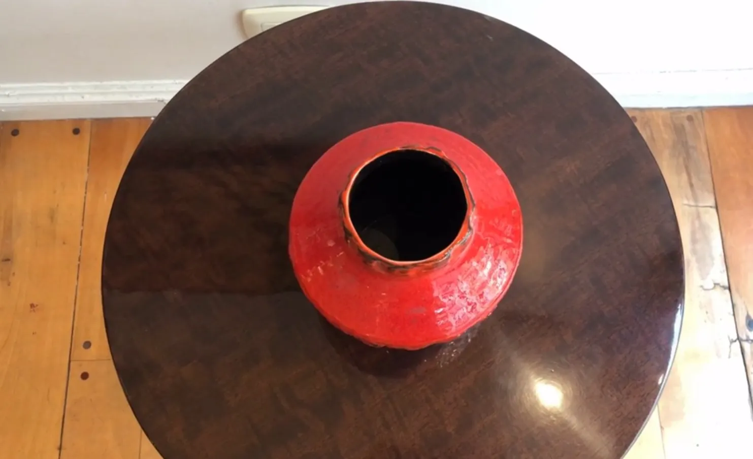 Alte rote Keramikvase in runder Form auf einem Holztisch.