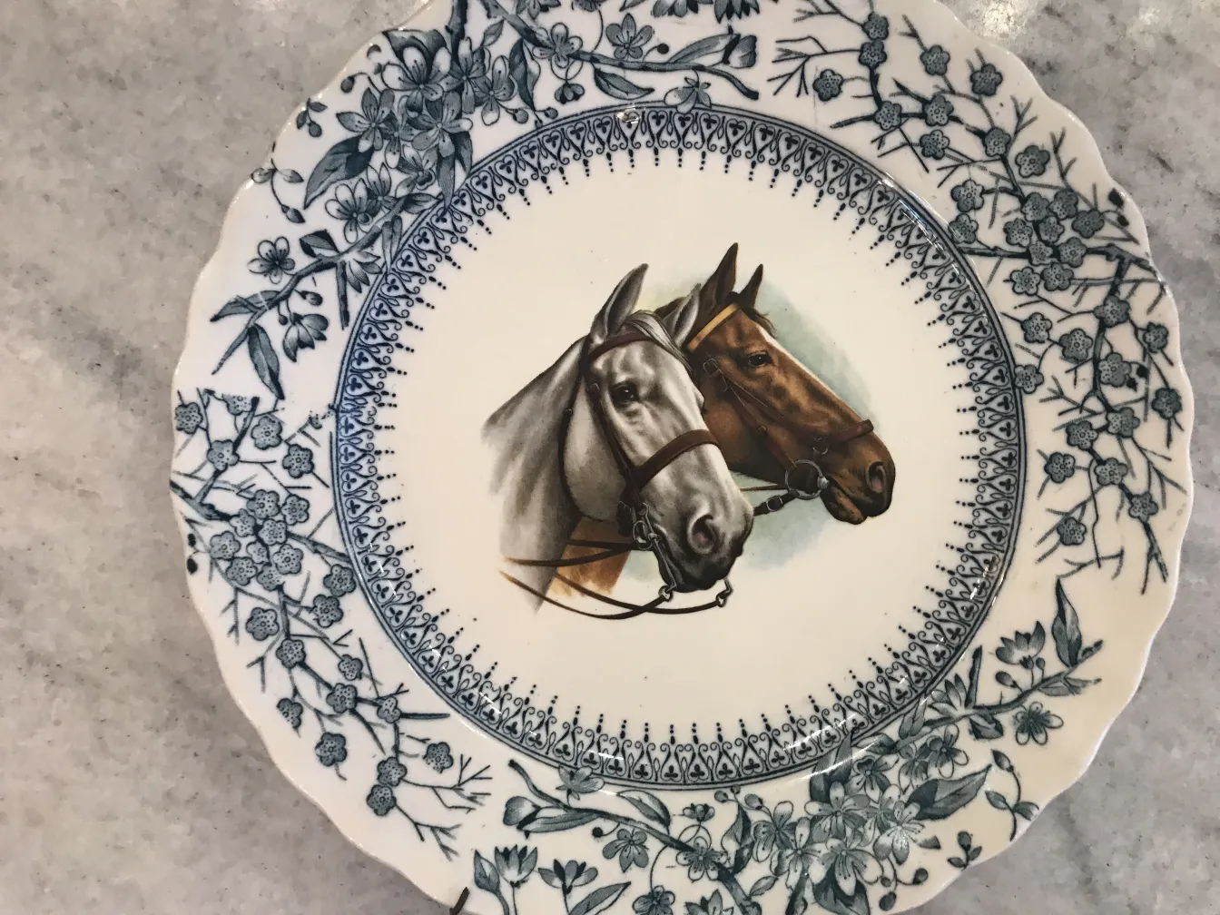 Antiker Keramikteller mit Pferden und blauen Blumendetails.