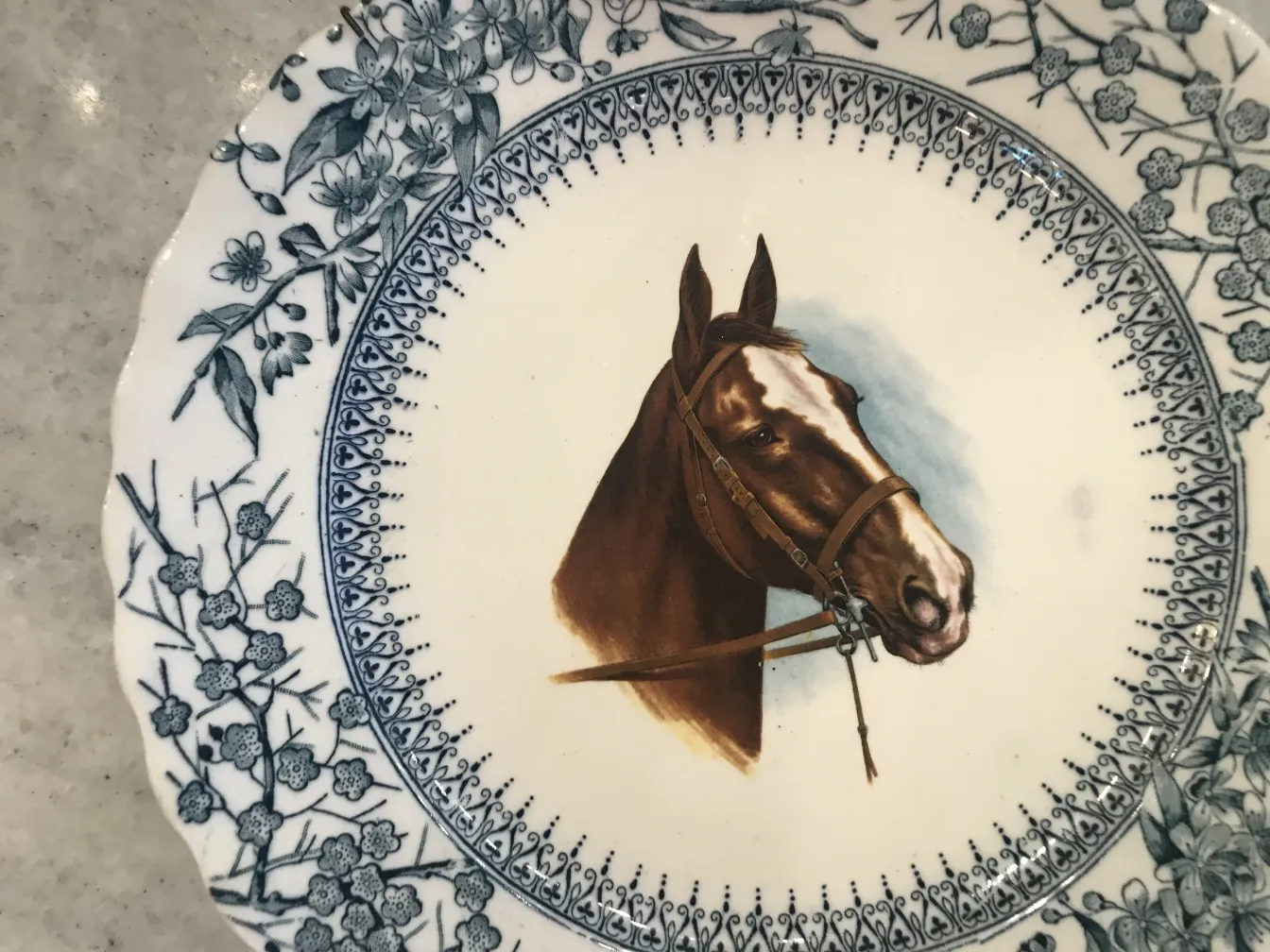 Antique ceramic plate featuring a brown horse image, decorated with blue flowers.