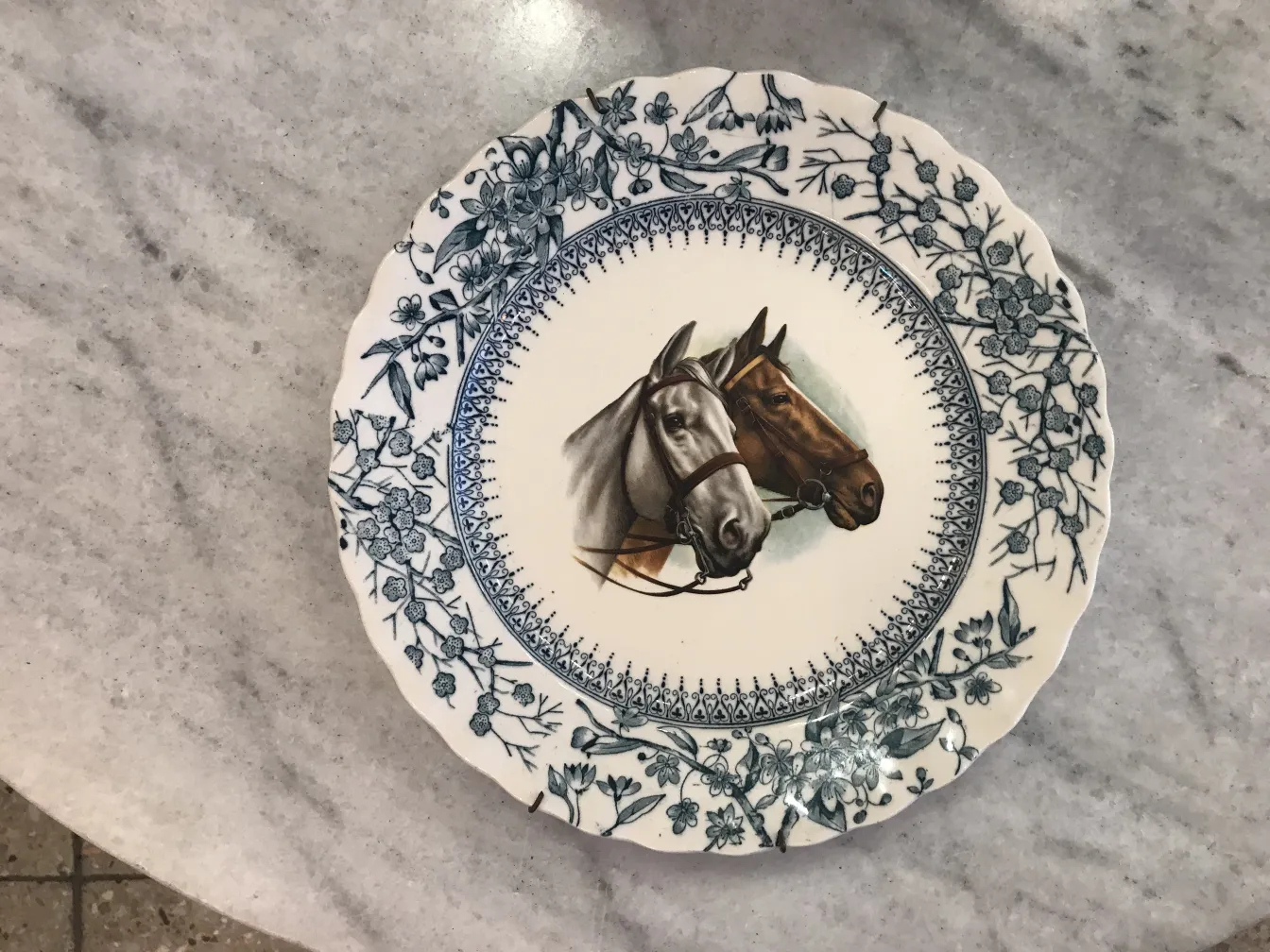 Antique ceramic plate featuring horses. Set against a light marble surface.