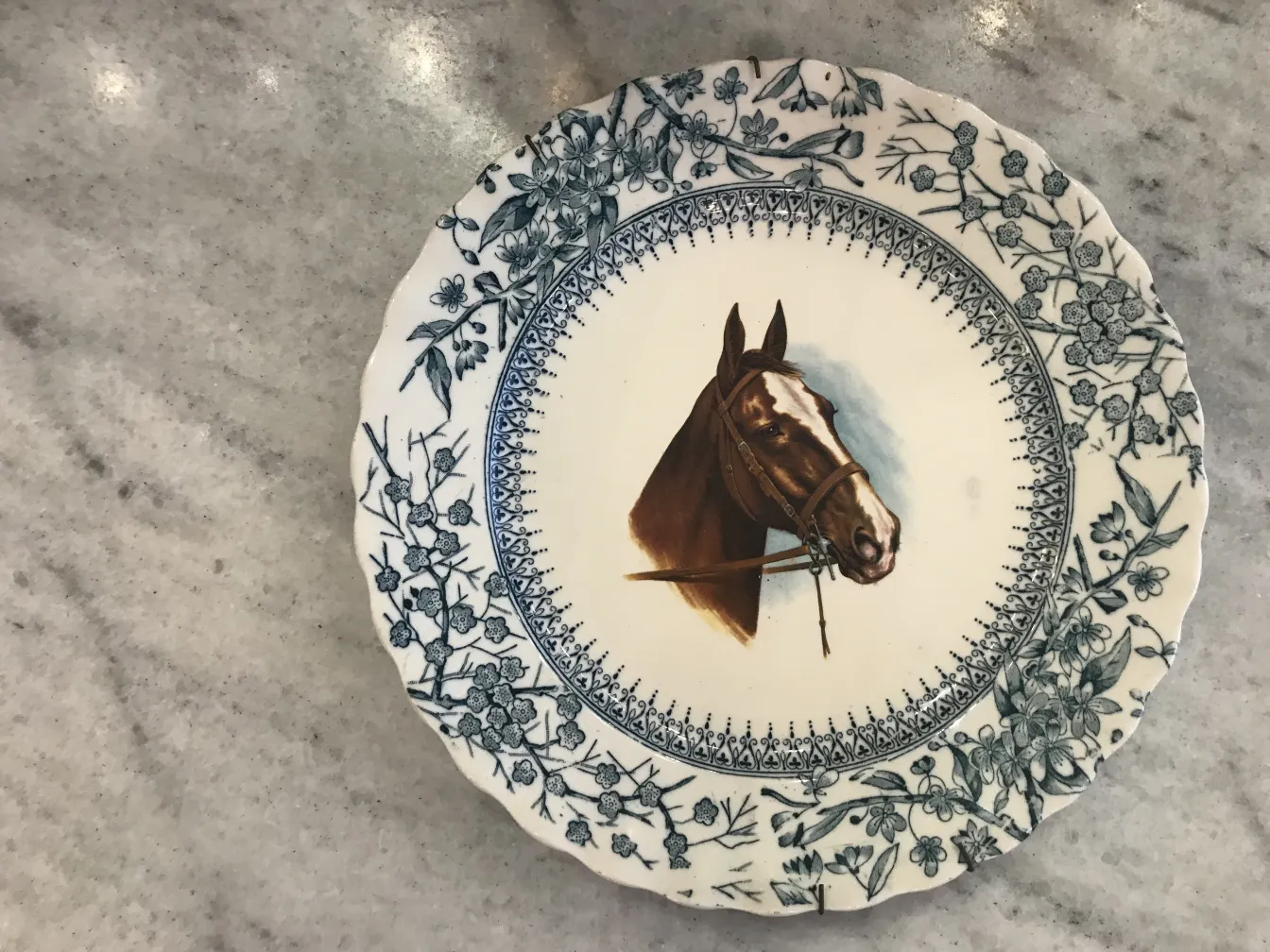 Prato de cerâmica antiga com imagem de um cavalo, decorado com flores azuis.