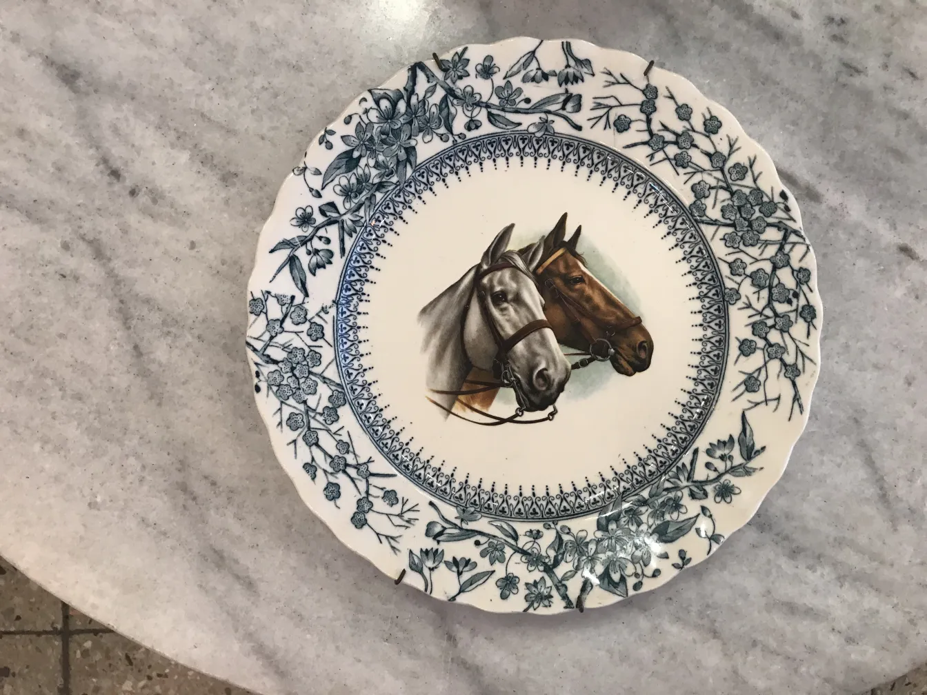 Antique ceramic plate featuring two horses and blue floral decorations.
