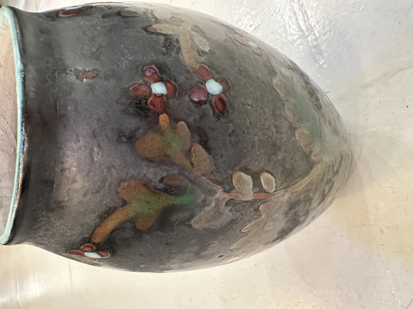 Vaso de cerâmica antiga com desenho floral em tons escuros.