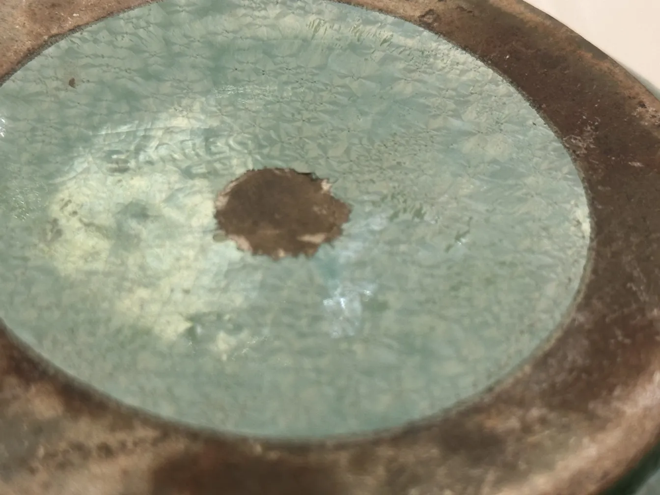 Detalhe de uma cerâmica antiga com brilho, mostrando textura irregular e um ambiente clássico.