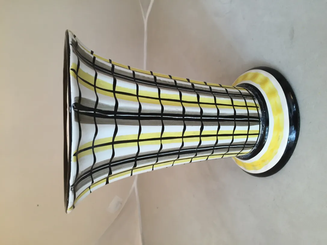Vase en céramique ancienne avec un motif noir et blanc et des détails jaunes, placé sur une surface claire.
