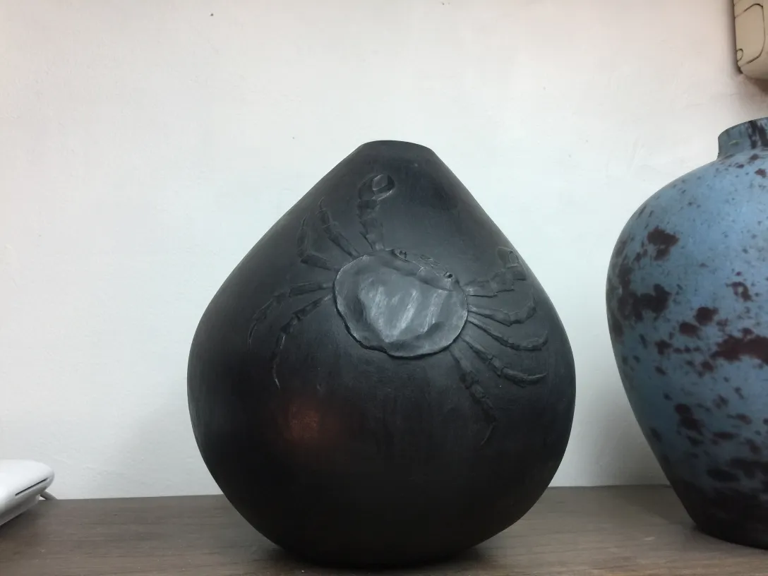 黒い陶器の花瓶にカニのデザイン、エレガントな環境に置かれています。