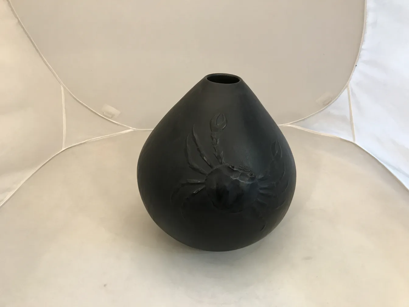 Antique ceramic vase decorated with a black crab, neutral background.