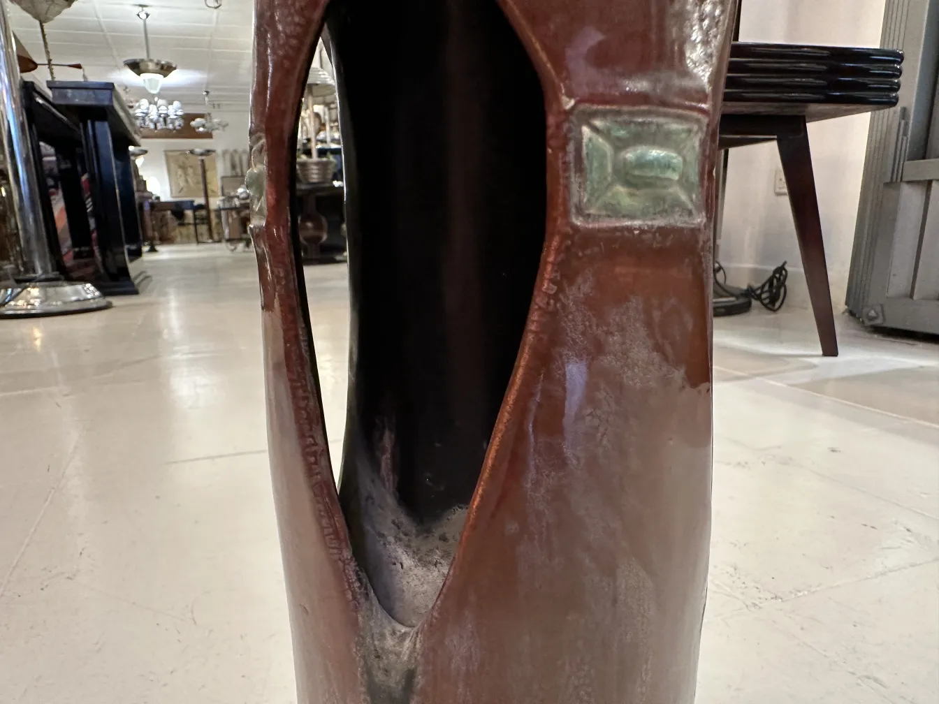 Vaso de cerámica antigua con abertura y detalles decorativos en un ambiente estilo clásico.