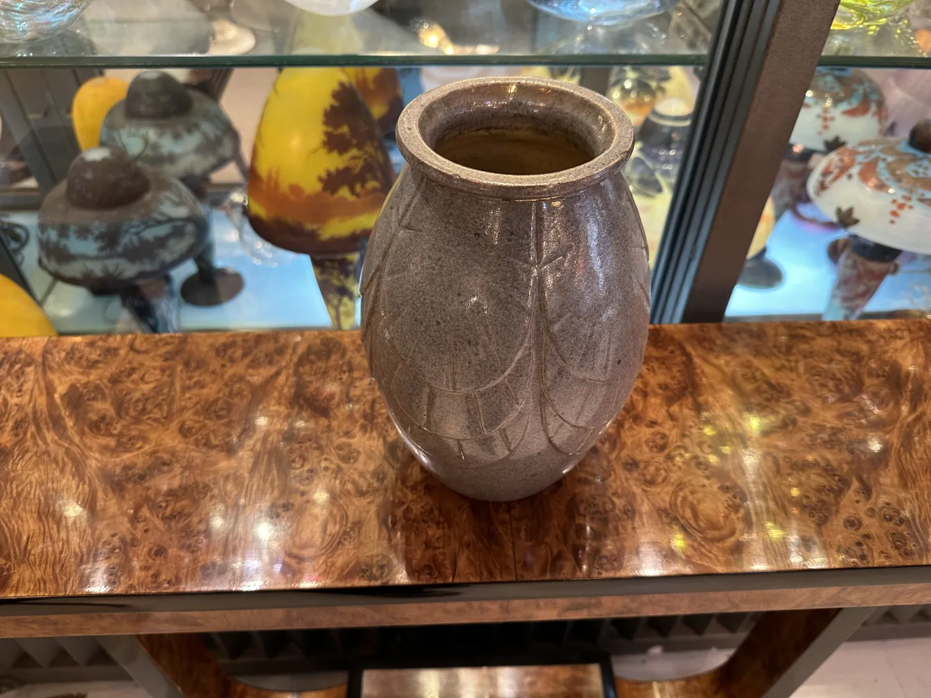 Jarrón de cerámica antigua con decoración sutil, fondo con otros objetos variados.