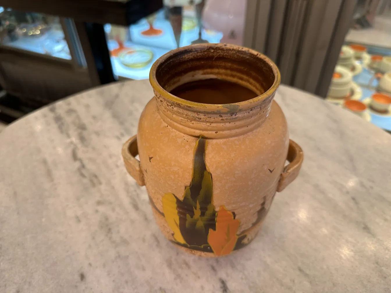 Vase en céramique ancienne avec un design naturel dans des tons terreux, posé sur une table avec un arrière-plan flou.