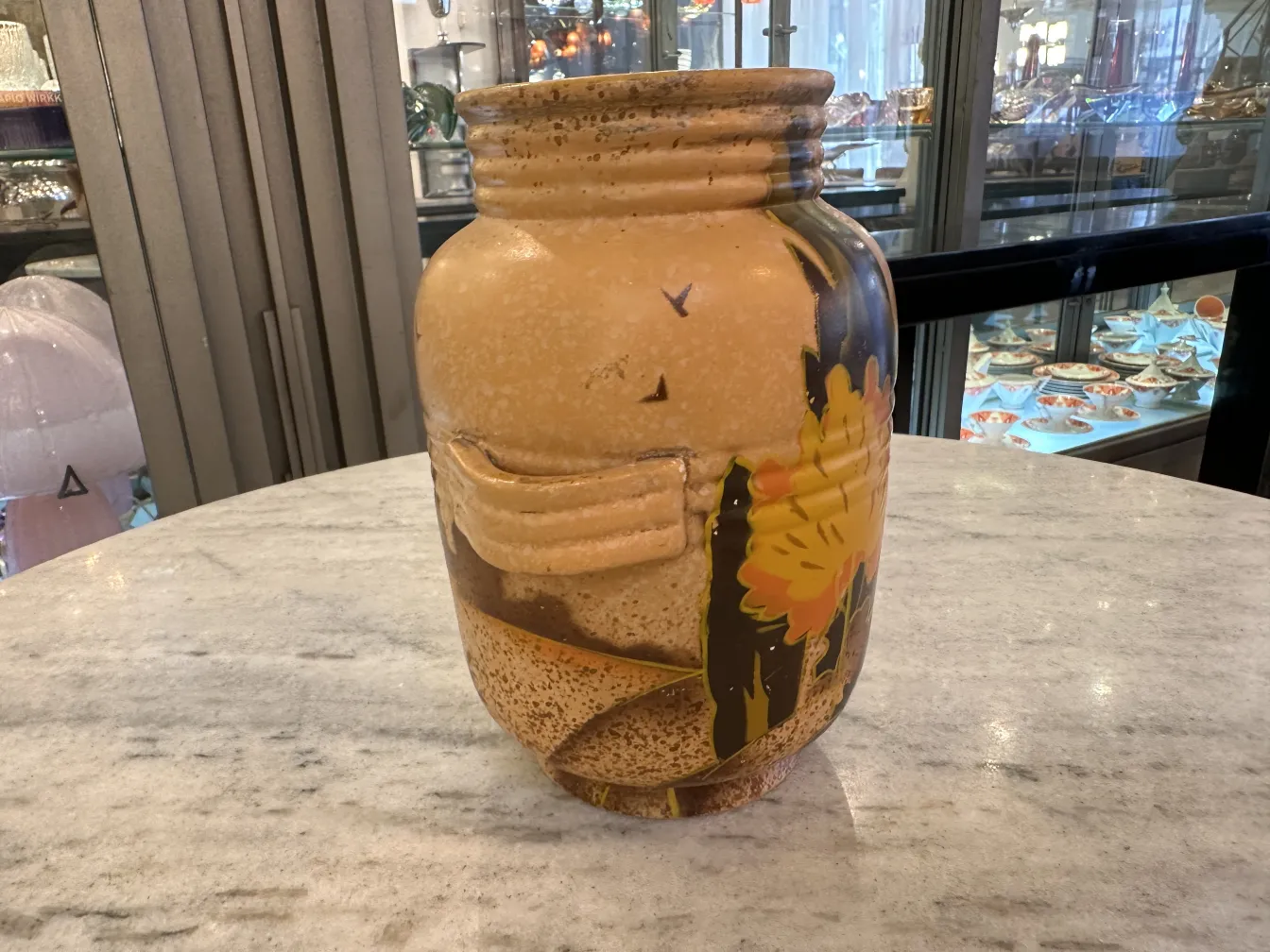 Vaso in ceramica antica con decorazione floreale vivace in toni caldi su uno sfondo chiaro.