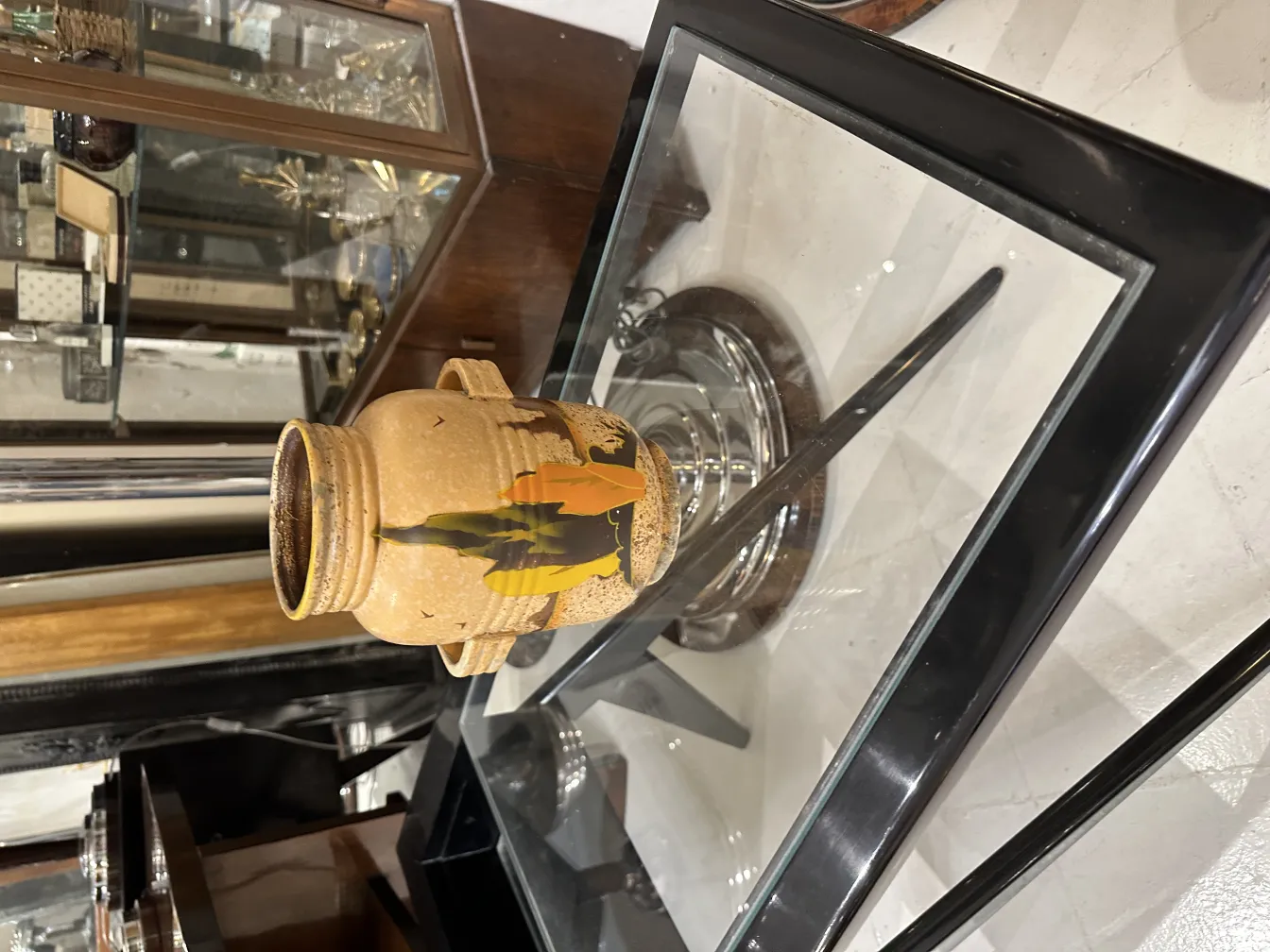 Vaso antico in ceramica decorato con motivi di foglie e colori caldi, in un ambiente elegante.