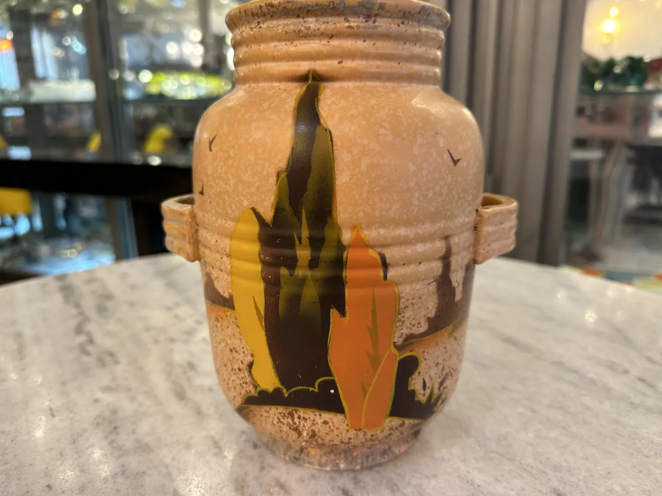 Vaso di ceramica antica con paesaggio dipinto in colori caldi.