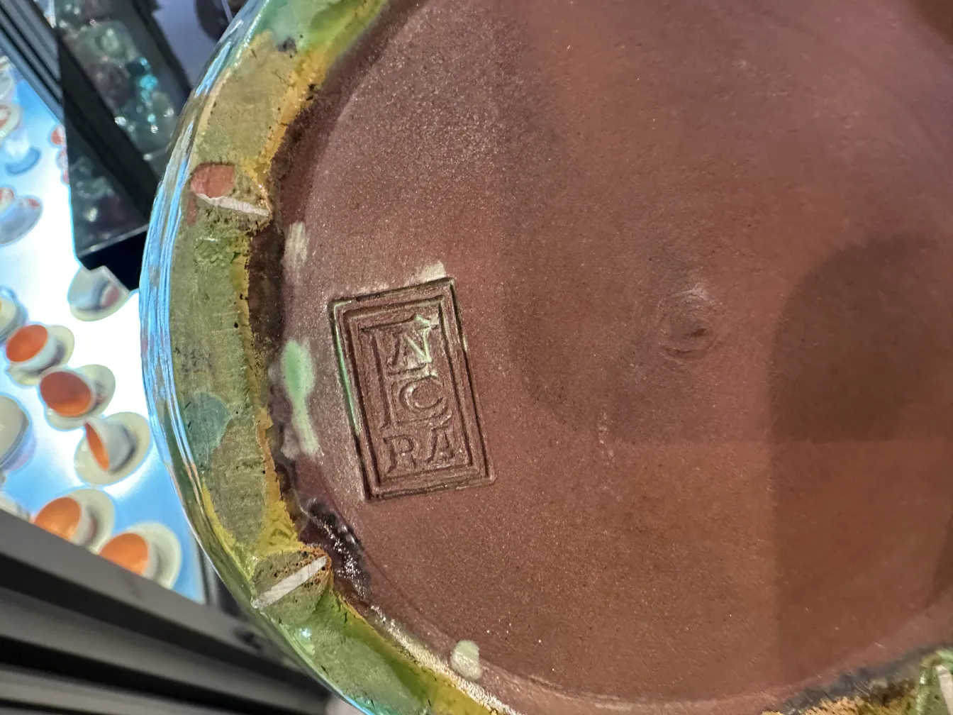 Taza de cerámica antigua con decoraciones coloridas y un sello en la base.