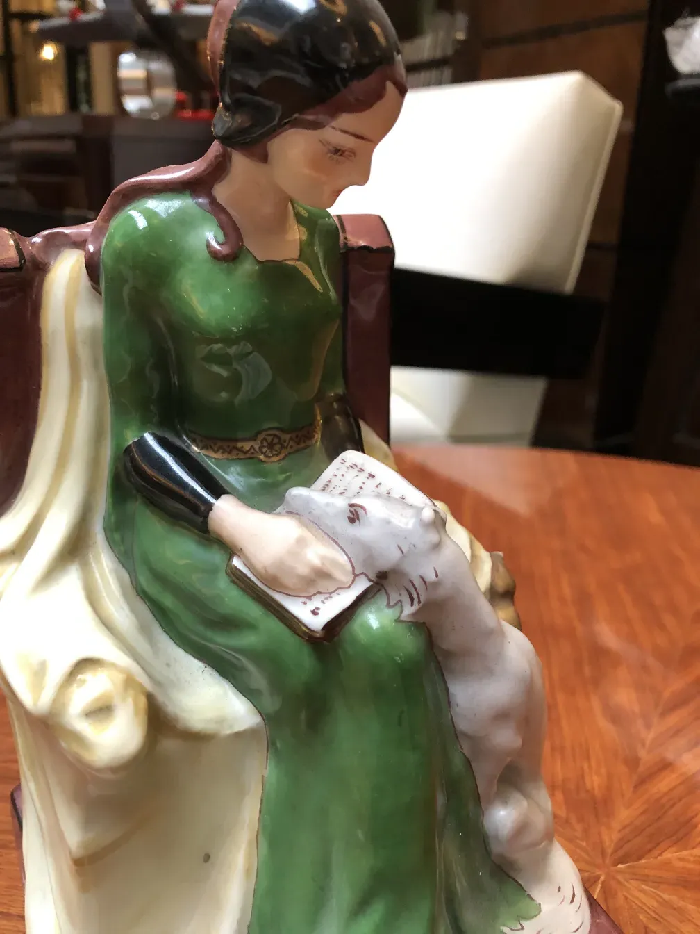 Figura de cerâmica antiga de mulher sentada em uma cadeira lendo.