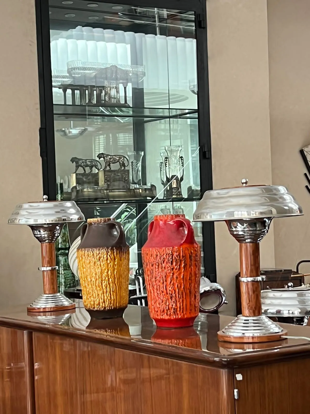 तीन प्राचीन मिट्टी के पात्र गर्म रंगों में एक मेज पर। पृष्ठभूमि में कांच की शेल्फ।