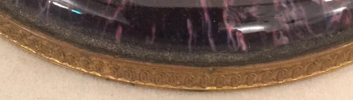 Cerâmica antiga com borda decorativa dourada e tons escuros.