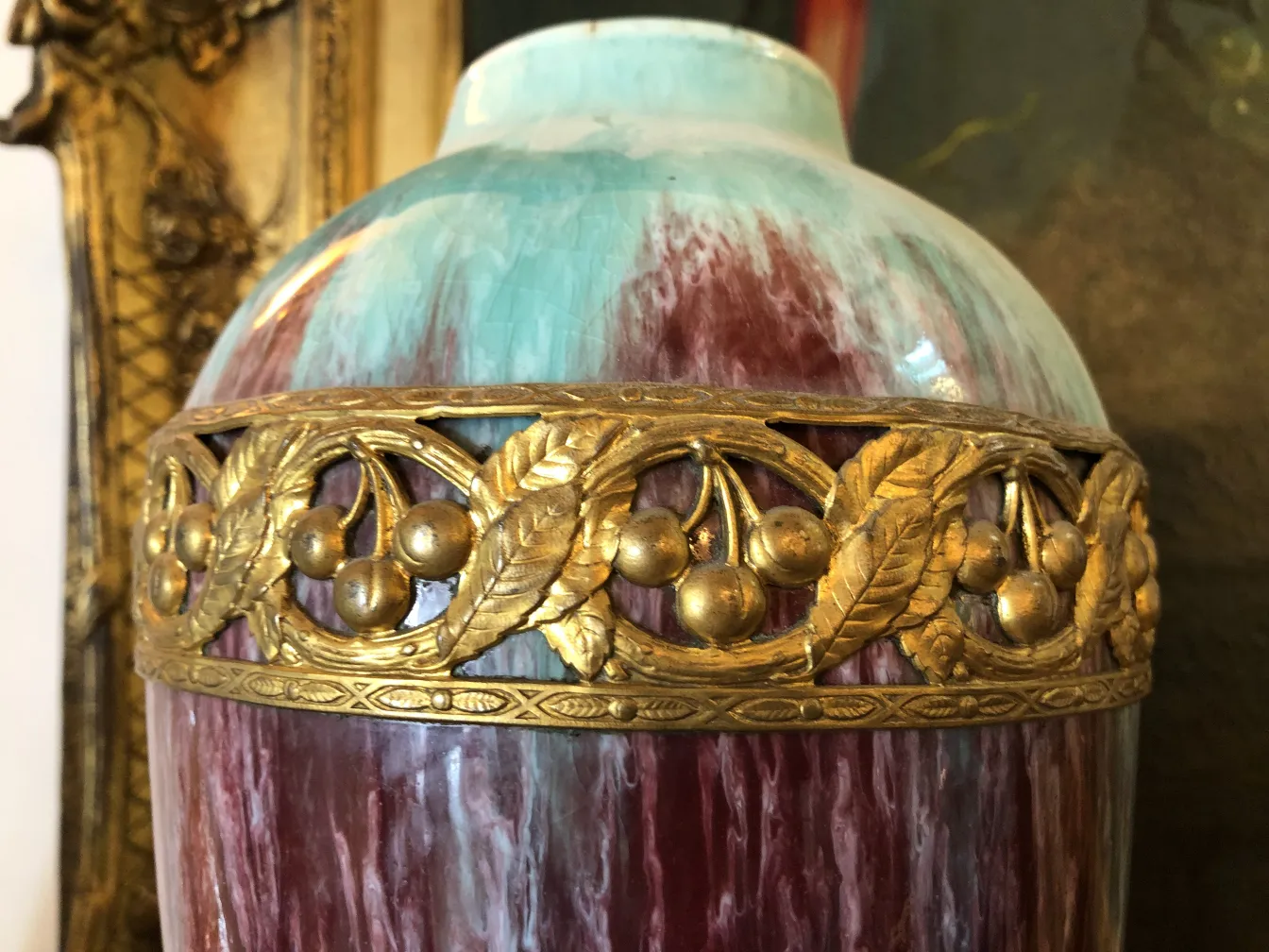 Vaso de cerâmica antiga com tons azuis e vermelhos, adornado com elementos decorativos elevados em dourado.