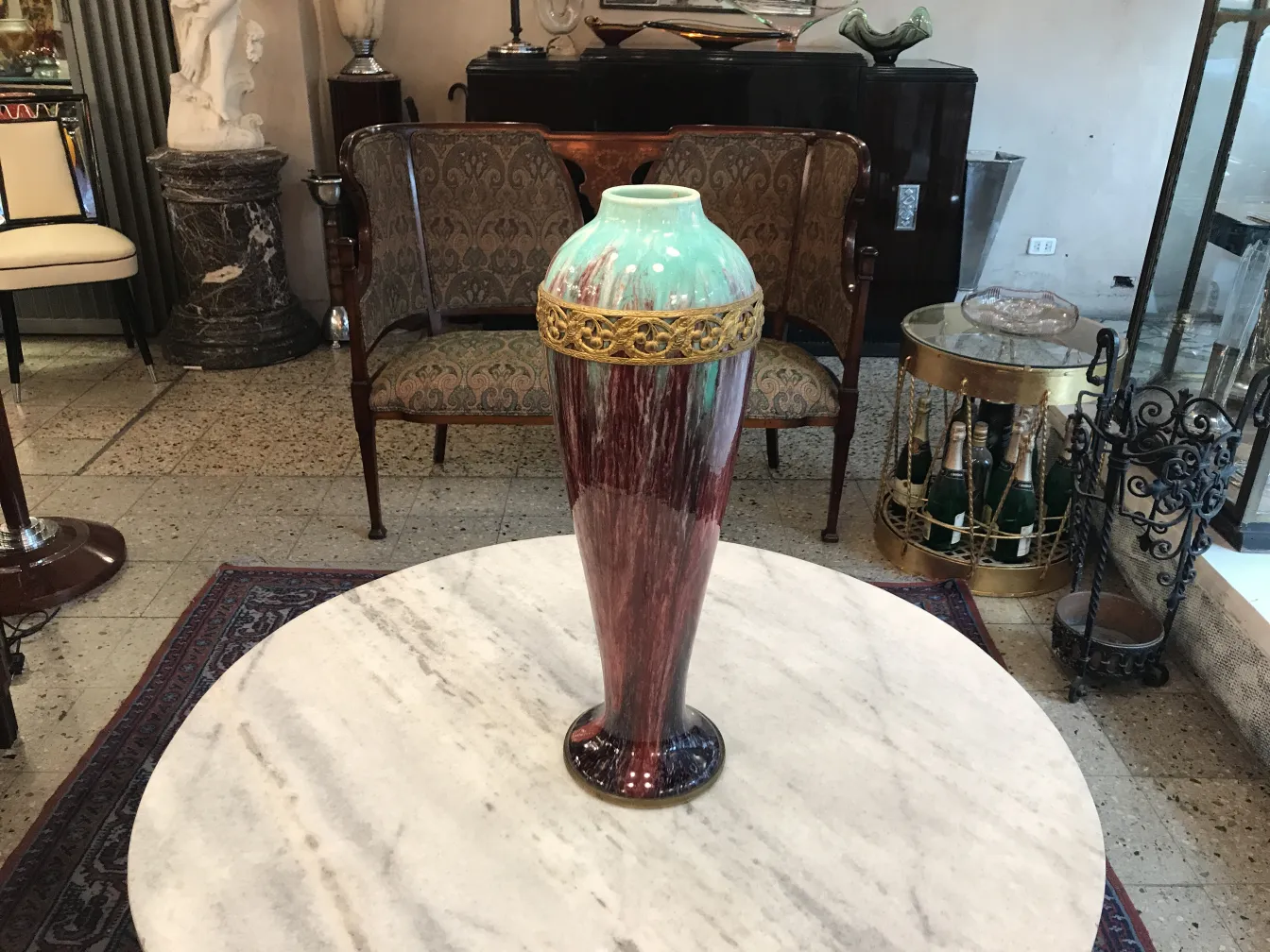 金の詳細と緑と赤のトーンを持つ古い陶器の花瓶が大理石のテーブルの上に置かれています。