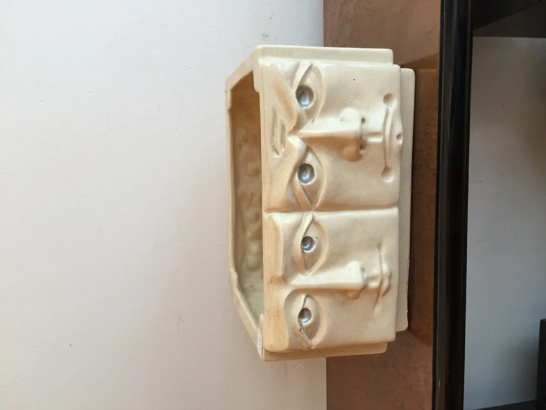 Antike Keramikskulptur mit Reliefgesichtern, weißer Hintergrund.