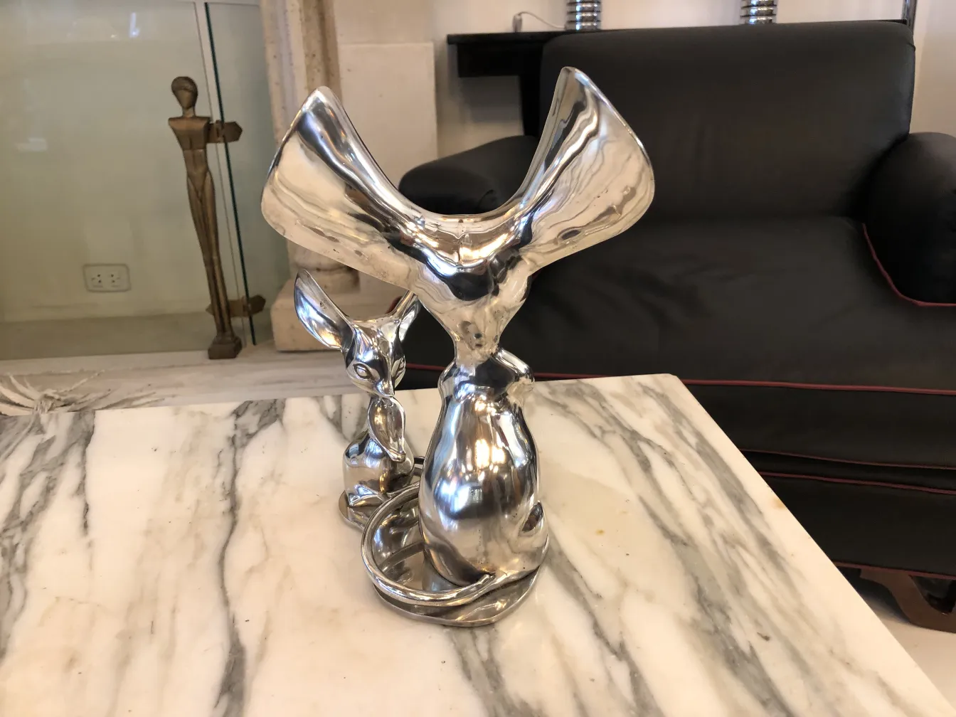 Antique sculpture with organic shapes in shiny metal, with a small figure beside it in an elegant setting.