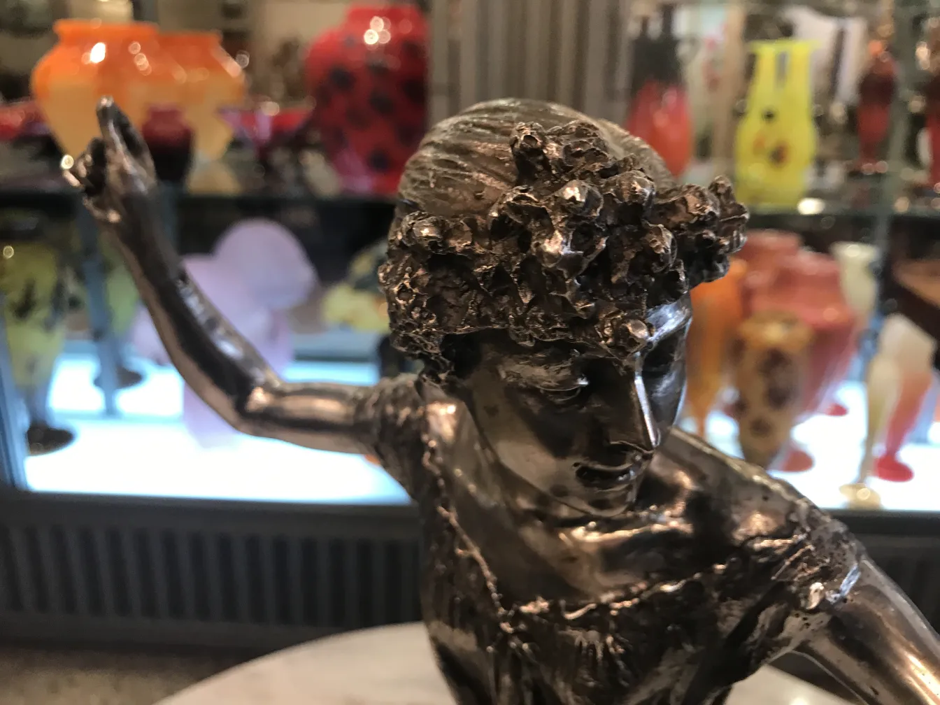 Alte Skulptur einer Frau mit blumenverzierten Haaren, umgeben von bunten Vasen.