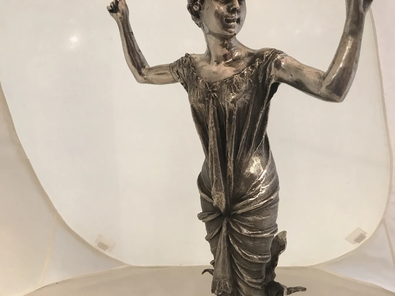 Antique sculpture of an artistic figure, featuring intricate dress details and arms in motion.