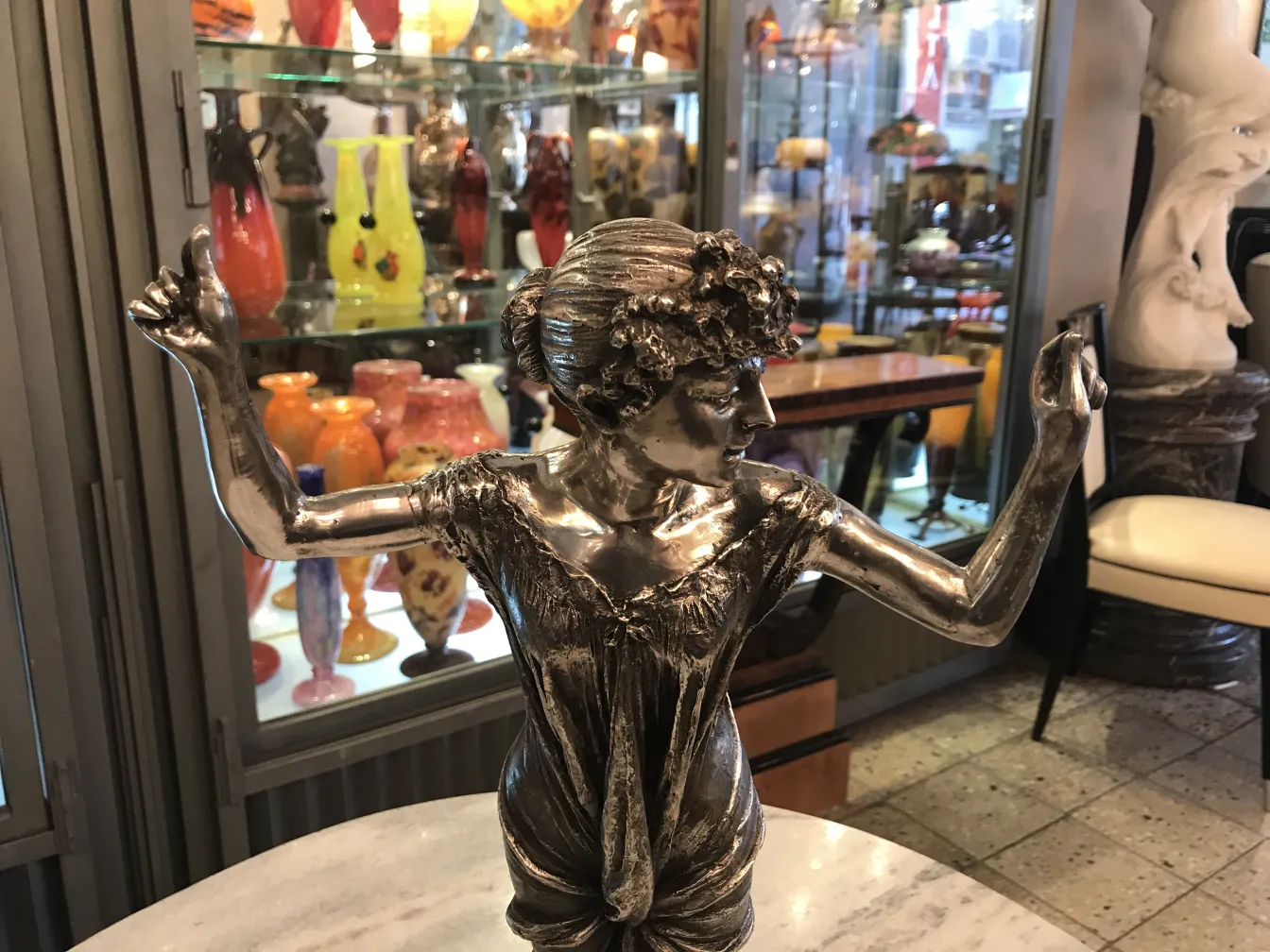 Scultura antica di una figura femminile con le braccia sollevate, circondata da vasi colorati.