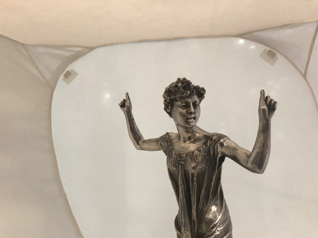 Scultura antica di figura femminile con mani alzate su sfondo neutro