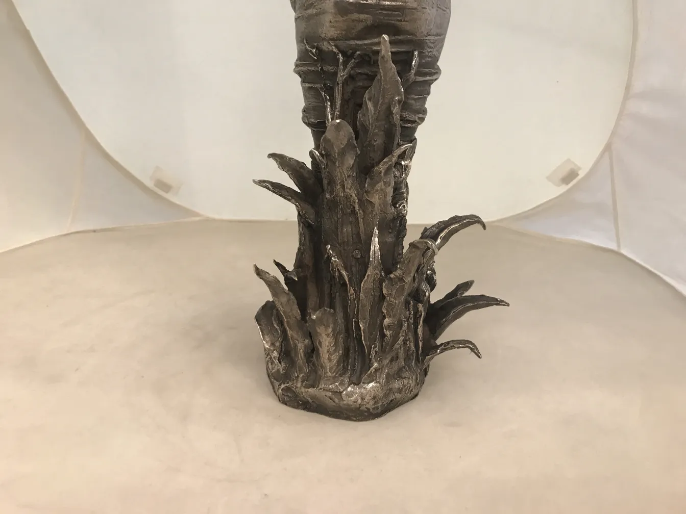 Scultura antica con basi simili a foglie su sfondo bianco.