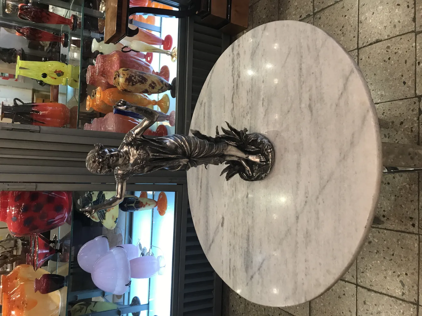 Antike Figurenskulptur auf einem Marmortisch mit buntem Hintergrund.