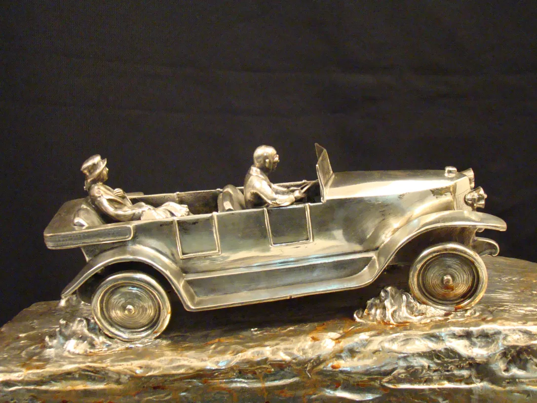 Sculpture ancienne de voiture avec des passagers détaillés.