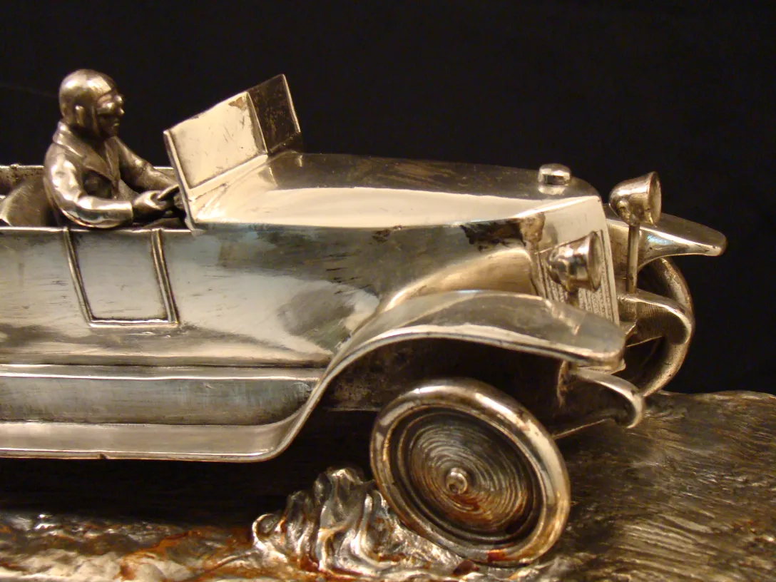 Sculpture ancienne d'une voiture stylisée avec un conducteur, brillante et détaillée.
