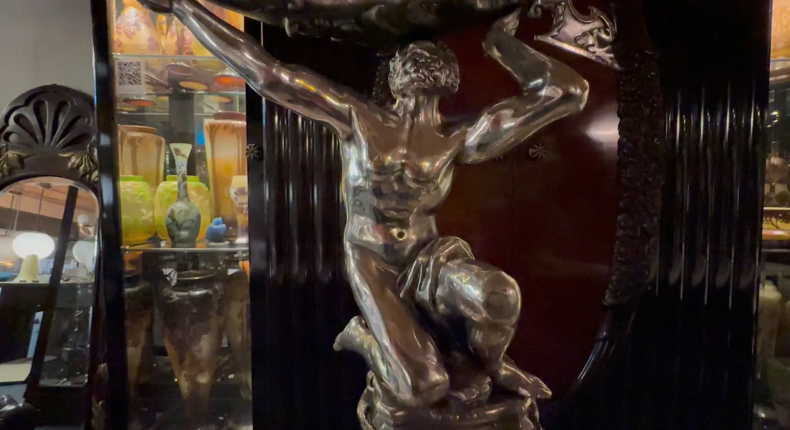 Antike Skulptur einer menschlichen Figur, die einen Gegenstand hält, Hintergrund mit verschiedenen Antiquitäten.