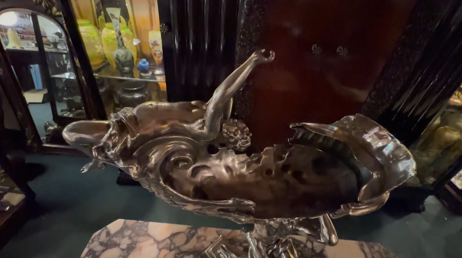 Antike Skulptur, die eine mythologische Szene mit metallischen Details darstellt, umgeben von Antiquitäten.