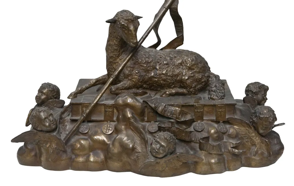 Sculpture ancienne d'un agneau sur un livre, entourée d'anges.