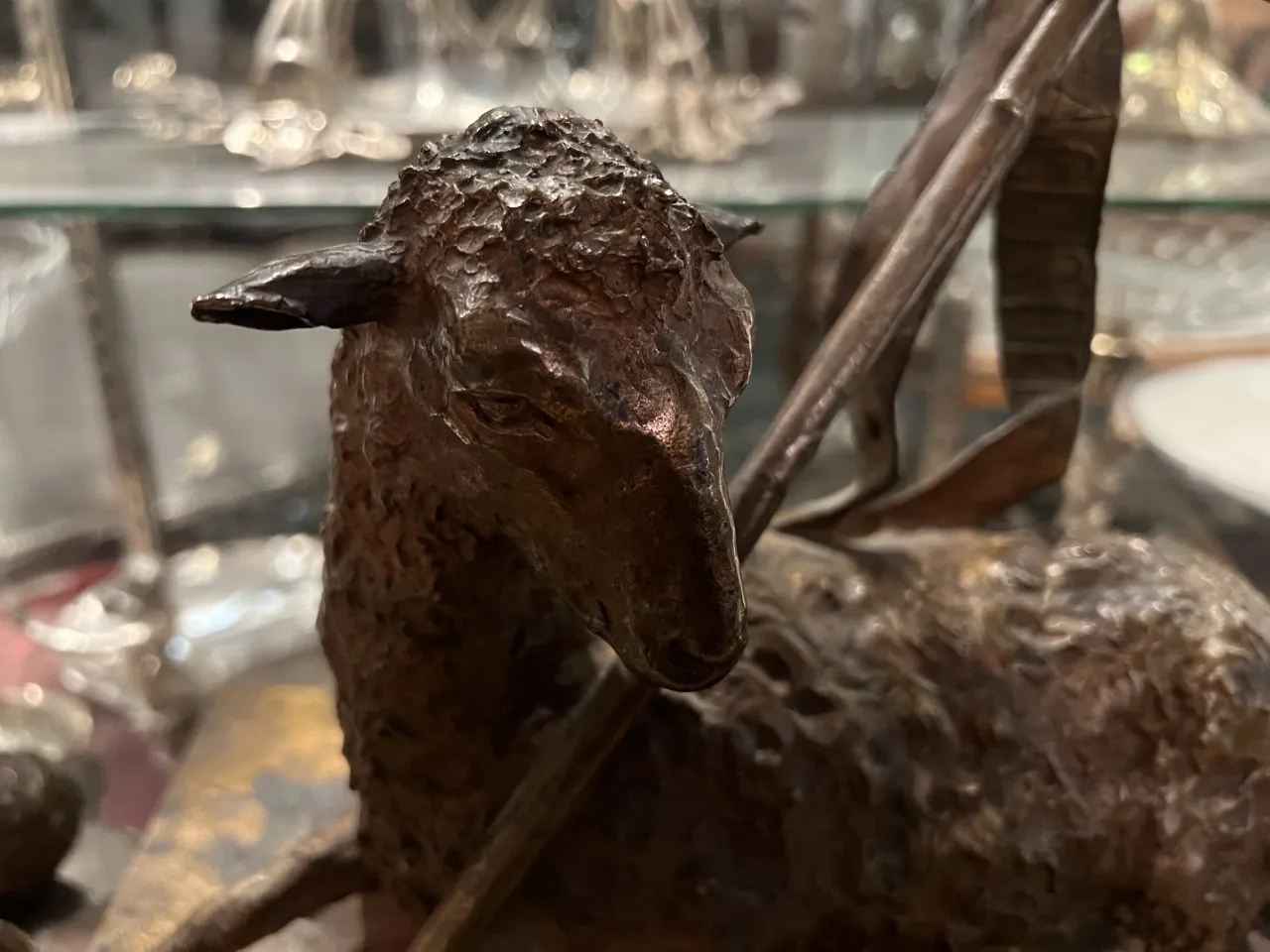 Scultura antica di una pecora con dettagli testurizzati e un arco.