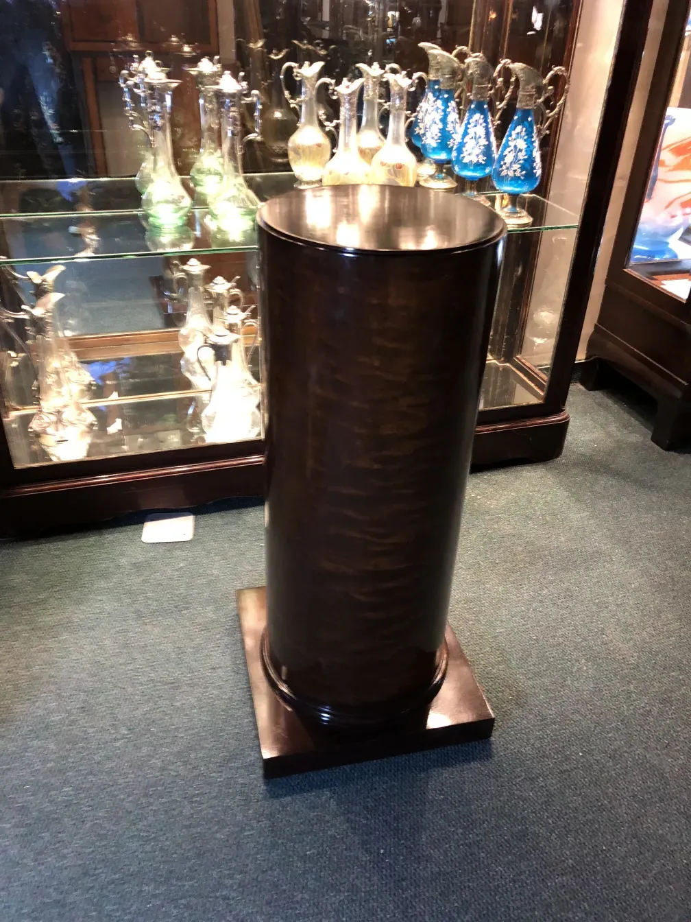 Antigua columna decorativa con superficie brillante y base sólida, rodeada de figuras de cristal.